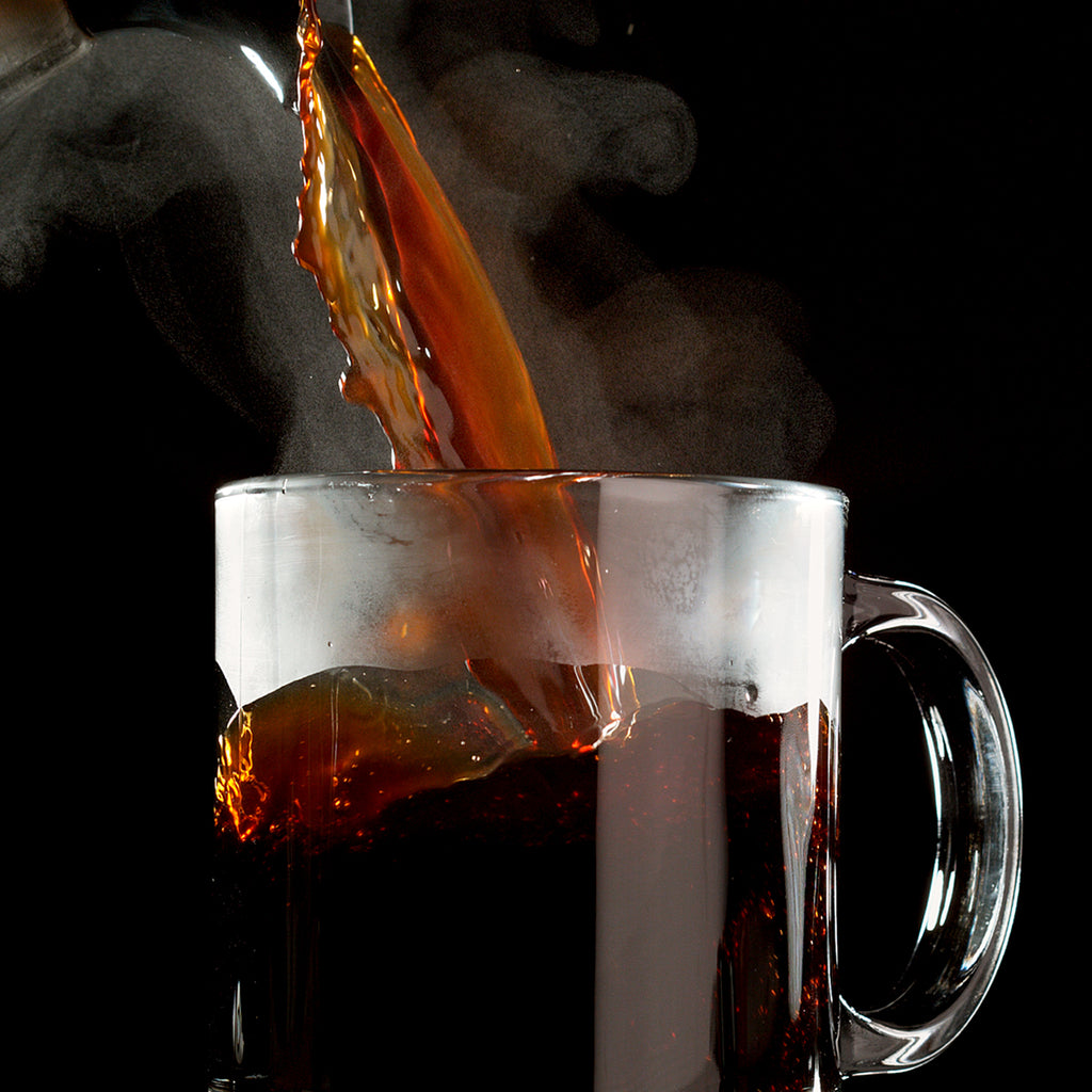 Hot coffee, made from Chock full o'Nuts 100% Colombian - Single-Serve Pods - Medium, is being poured into a clear glass mug, creating steam against a black background.