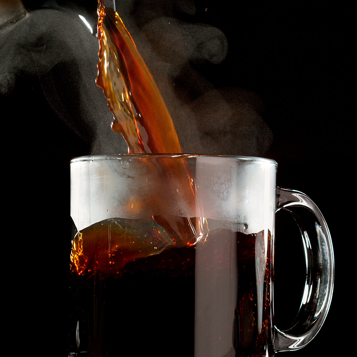 Hot Colombian coffee, brewed to perfection with Chock full o'Nuts 100% Colombian - Single-Serve Pods - Medium, is being poured into a clear glass mug, with steam rising elegantly against a black background.