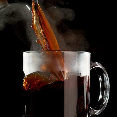 Hot Colombian coffee, brewed to perfection with Chock full o'Nuts 100% Colombian - Single-Serve Pods - Medium, is being poured into a clear glass mug, with steam rising elegantly against a black background.