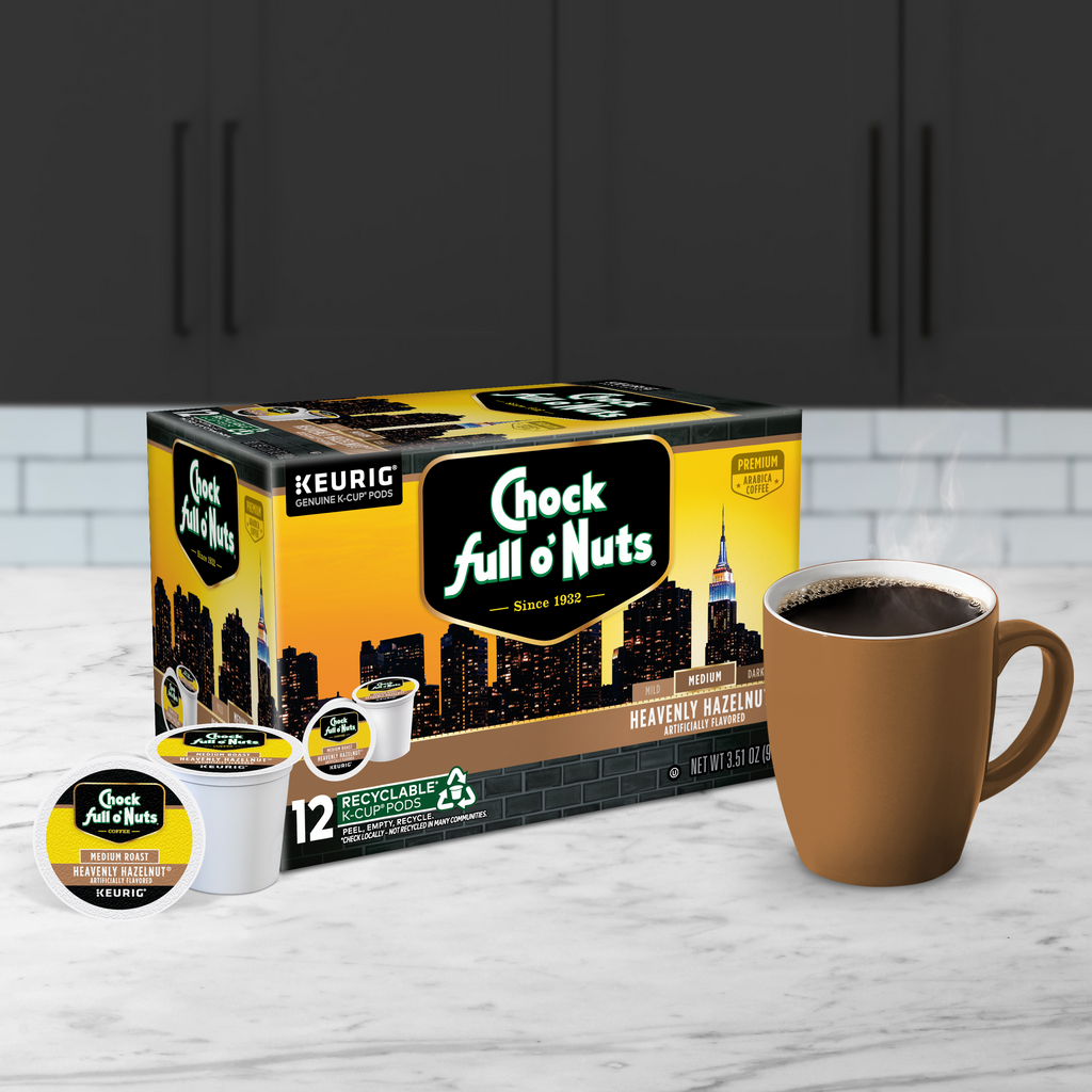 A box of Chock full o'Nuts Heavenly Hazelnut Medium Roast Keurig K-Cup® Pods is on the kitchen counter, beside a steaming brewed coffee cup.