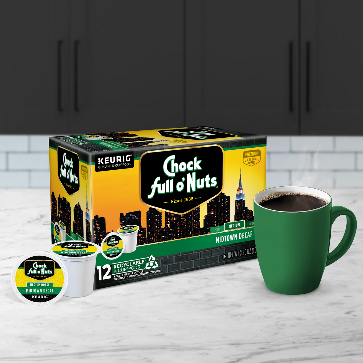 A box of Chock full o'Nuts Midtown Decaf - Keurig K-Cup Pods - Medium is placed next to a green mug filled with premium Arabica coffee, ready to be enjoyed, on a kitchen counter.