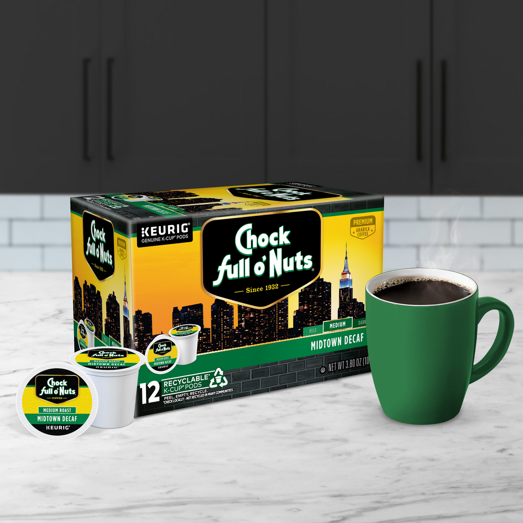 A box of Chock full o'Nuts Midtown Decaf - Keurig K-Cup Pods - Medium is placed next to a green mug filled with premium Arabica coffee, ready to be enjoyed, on a kitchen counter.