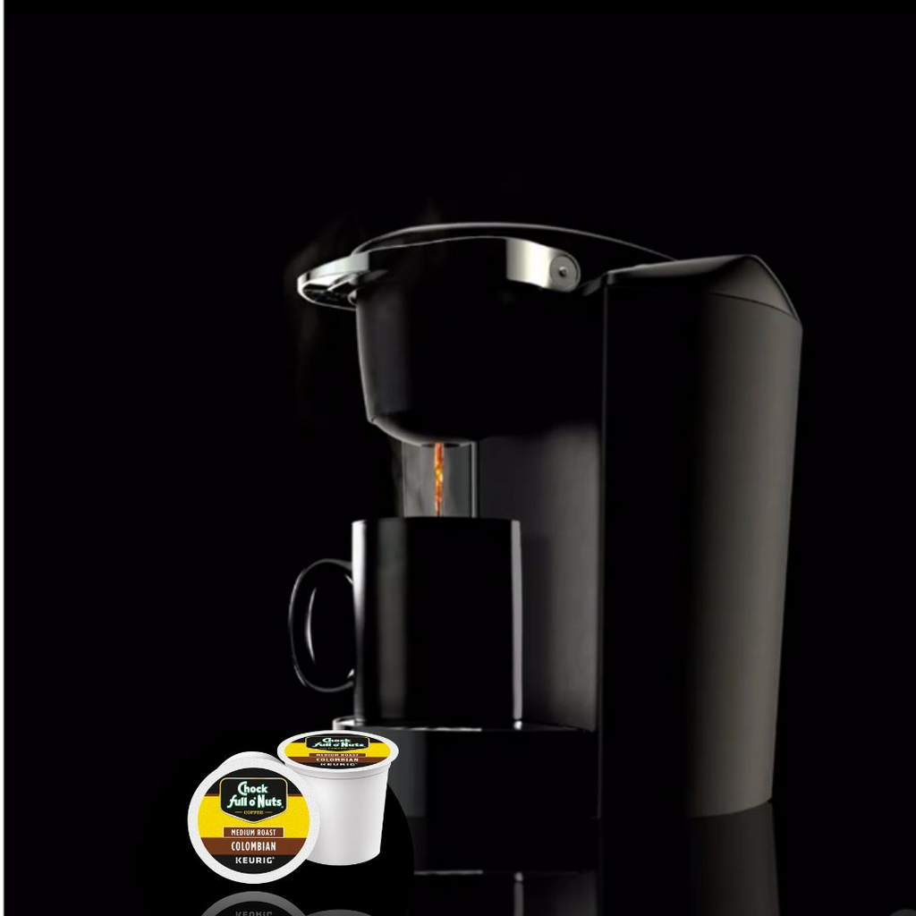 A Chock full o'Nuts black coffee maker brews Colombian - Keurig K-Cup® Pods Medium Roast coffee into a black mug. Two single-serve Chock full o'Nuts coffee pods are positioned in front of the machine.