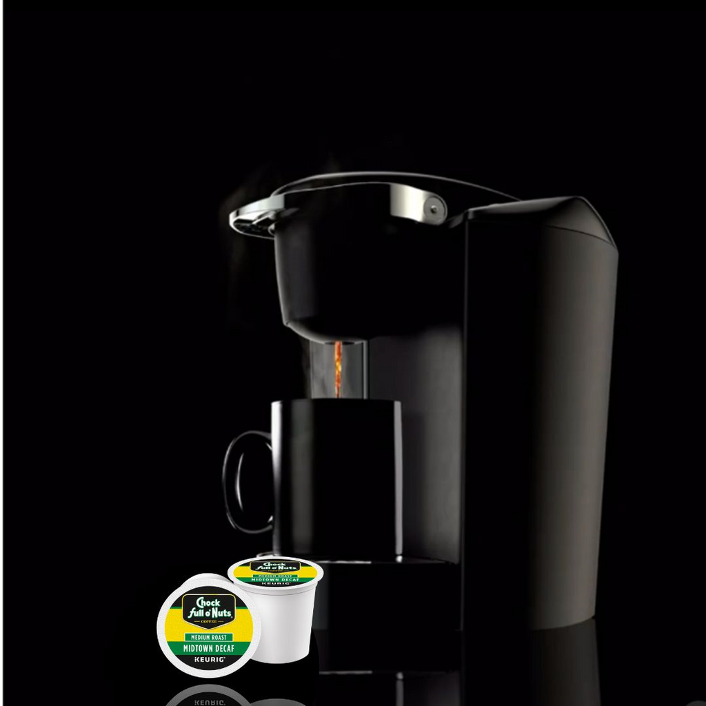 A coffee maker brews into a black mug, with two "Midtown Decaf - Keurig K-Cup® Pods - Medium" from the brand Chock full o'Nuts in the foreground against a dark background, accentuating the rich essence of premium Arabica coffee.