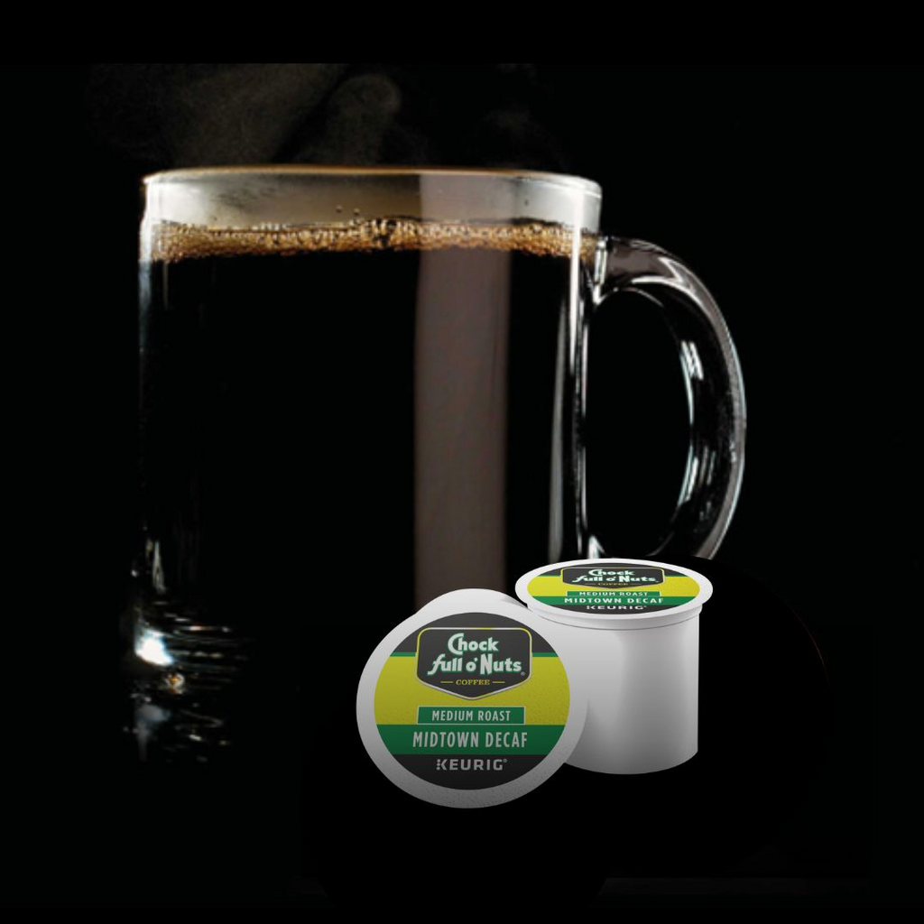 A clear mug filled with black coffee sits behind two green and white "Chock full o'Nuts" Midtown Decaf - Keurig K-Cup Pods, offering a rich taste of premium Arabica coffee.